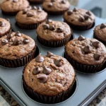 Tray of moist, high protein breakfast muffins topped with dark chocolate chips, cooling in a non stick muffin pan.